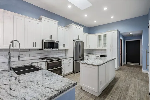 a kitchen with stainless steel appliances granite countertop a stove top oven a sink and a refrigerator