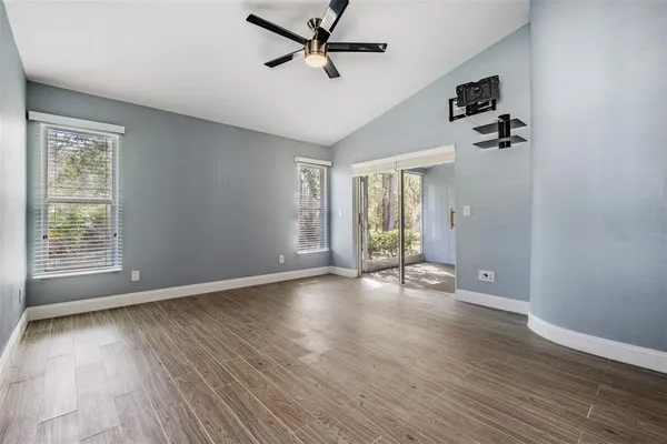 an empty room with wooden floor fan and windows