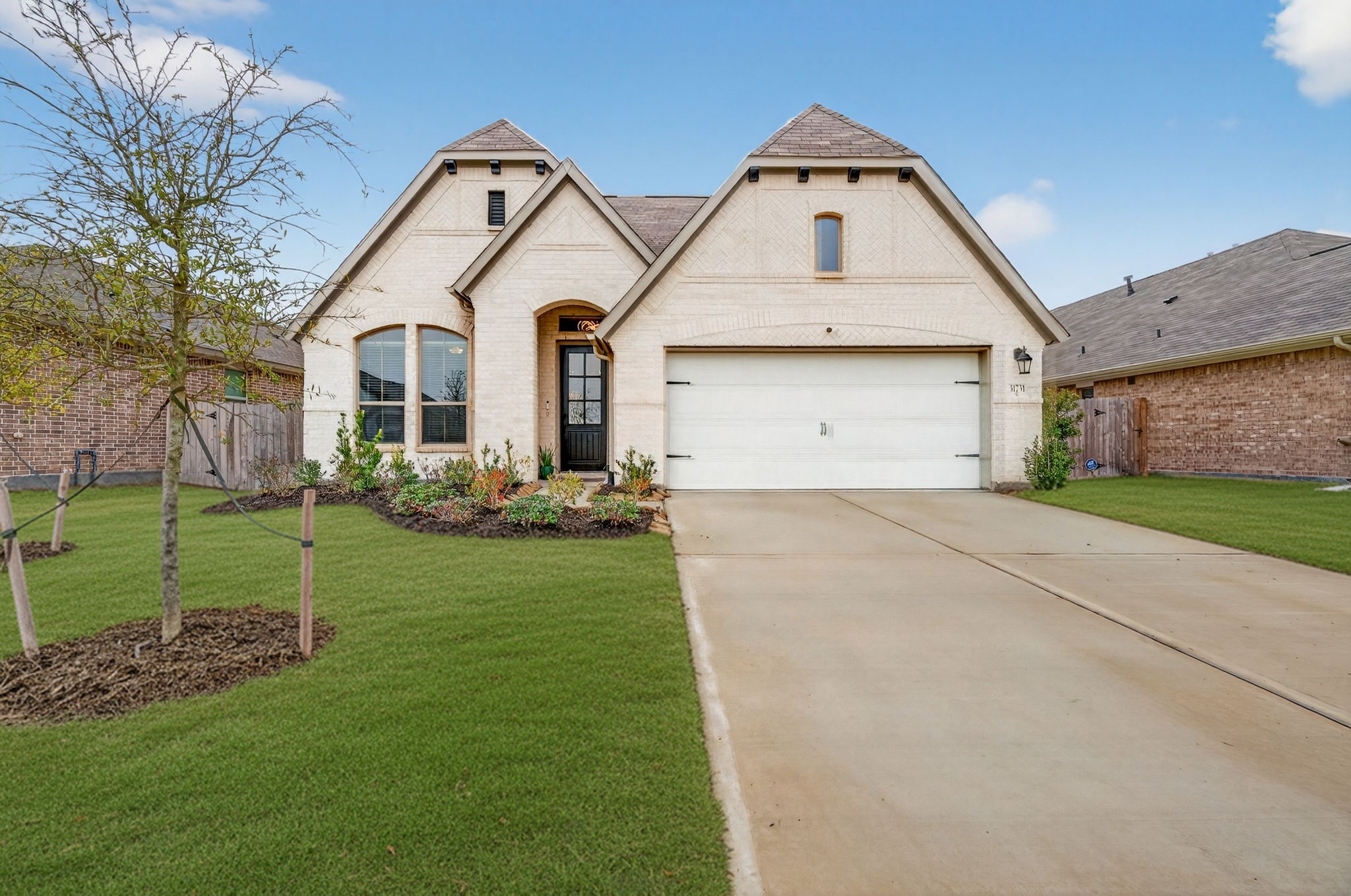 This is a charming single-story brick home with a gabled roof and a two-car garage. The well-maintained front yard features a neat lawn and landscaped flower beds, adding to its curb appeal.