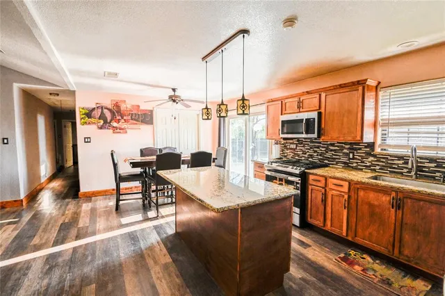 a kitchen with stainless steel appliances granite countertop a stove top oven a sink dishwasher a dining table and chairs with wooden floor