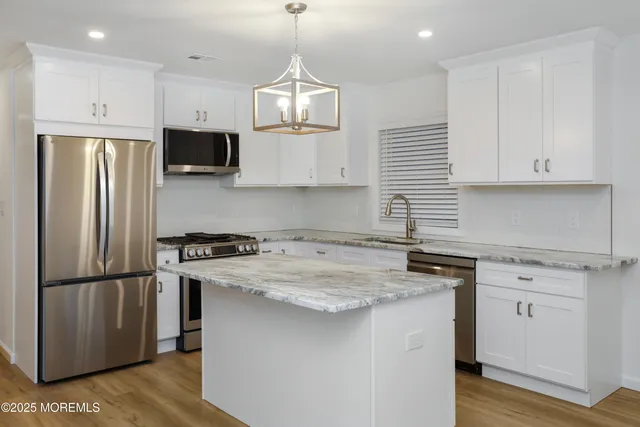 a kitchen with stainless steel appliances granite countertop a sink stove a refrigerator and white cabinets with wooden floor