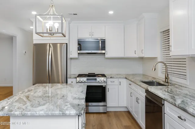 a kitchen with granite countertop a sink stainless steel appliances and white cabinets