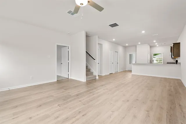 an empty room with wooden floor kitchen view and a window