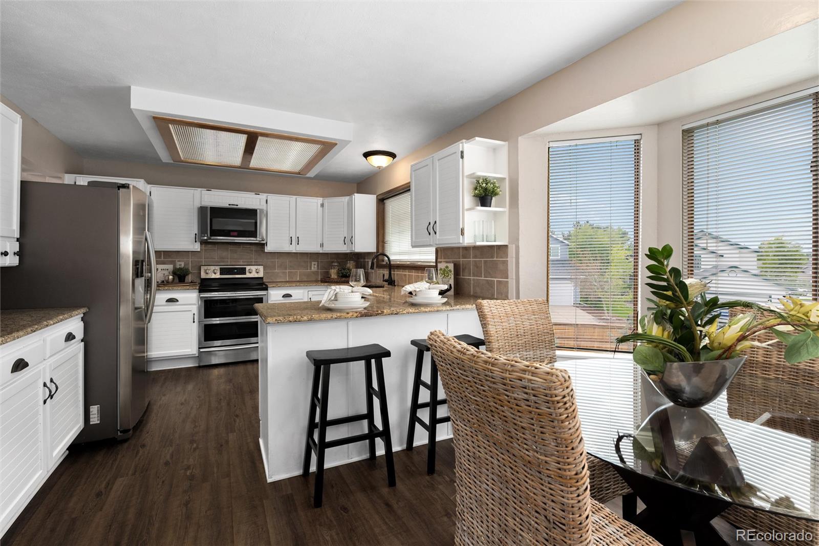 1225 East Goldsmith Drive Highlands Ranch, CO 80126 - Photo 12 of 40 a kitchen with stainless steel appliances kitchen island granite countertop a refrigerator a stove top oven a sink dishwasher and white cabinets with wooden floor