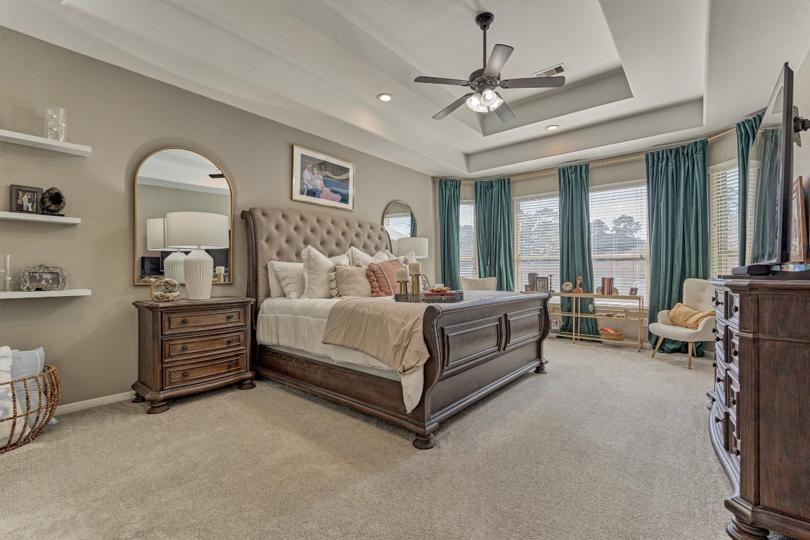 226 Hampton Glen Road Montgomery, TX 77356 - Photo 16 of 48 This spacious primary bedroom features a tray ceiling with a fan, large windows with elegant drapes, and plush carpeting.