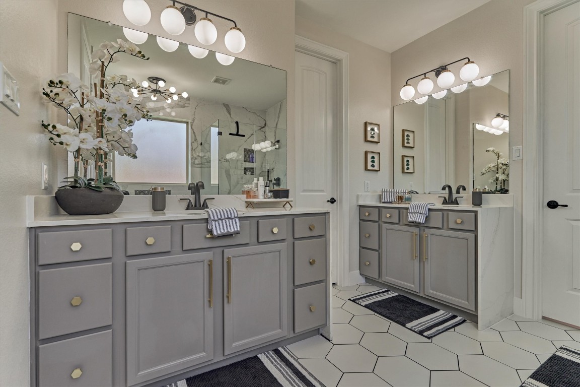 226 Hampton Glen Road Montgomery, TX 77356 - Photo 23 of 48 This bathroom features dual vanities with modern black fixtures. It has large mirrors, stylish lighting, and a spacious shower area. The hexagonal floor tiles add a contemporary touch, complemented by tasteful decor.