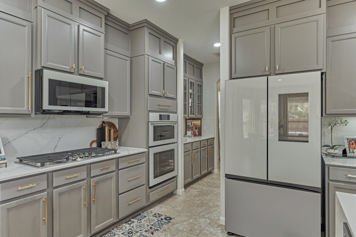 226 Hampton Glen Road Montgomery, TX 77356 - Photo 9 of 48 This modern kitchen features updated cabinetry with gold hardware and tiled flooring. It includes high-end appliances such as a built-in microwave, gas cooktop, dual ovens, and a stylish double-door refrigerator. The spacious layout offers ample storage and counter space, perfect for culinary enthusiasts.