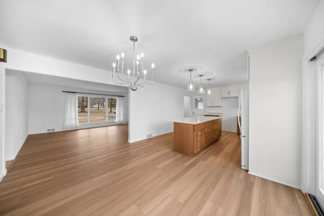 a view of an empty room and kitchen with wooden floor