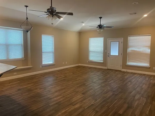 an empty room with wooden floor ceiling fan and windows