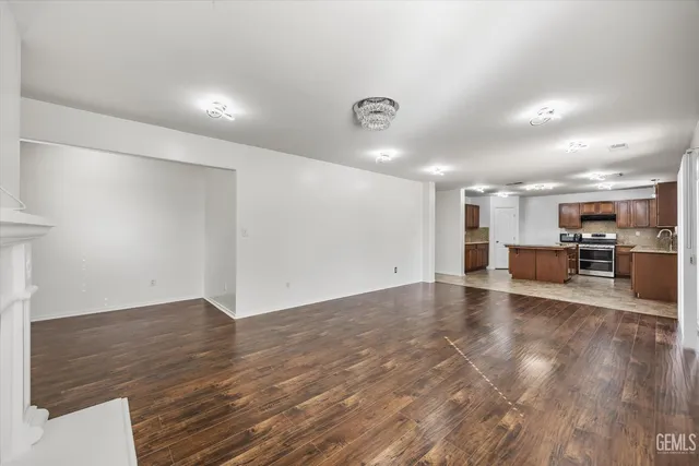 an empty room with wooden floor and kitchen view