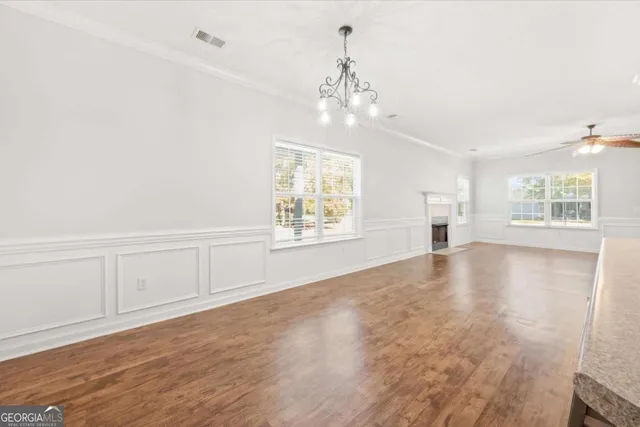 an empty room with wooden floor chandelier and windows