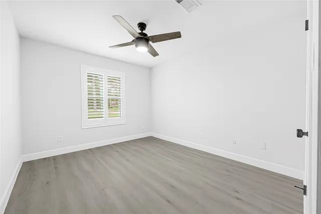 an empty room with wooden floor fan and windows