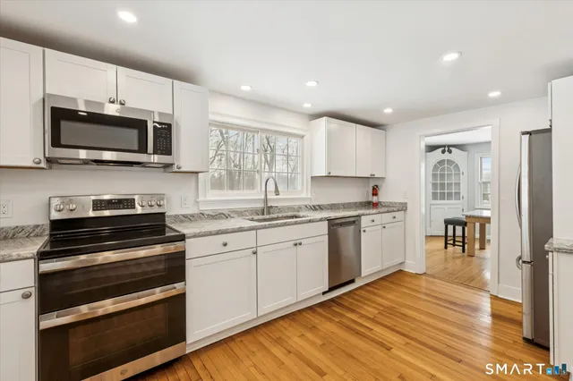 a kitchen with stainless steel appliances kitchen island granite countertop a stove top oven a sink dishwasher a refrigerator and white cabinets with wooden floor