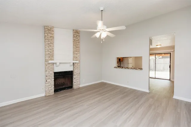 an empty room with wooden floor fireplace and ceiling fan