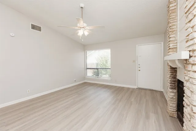 an empty room with wooden floor fan and windows