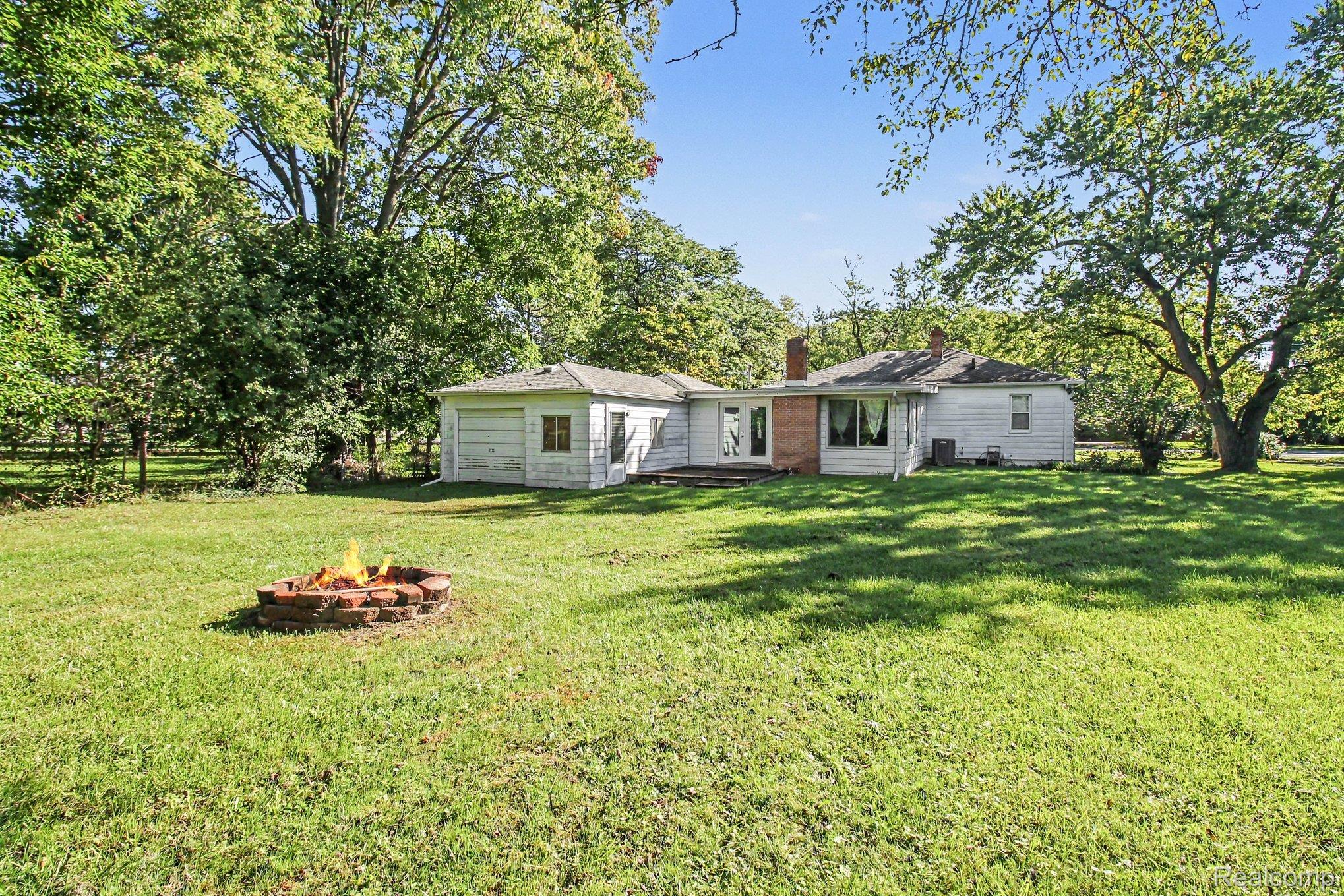 207 Elms Road Flushing, MI 48433 - Photo 24 of 30 Expansive green lawn with a brick fire pit, mature trees, and a detached garage structure