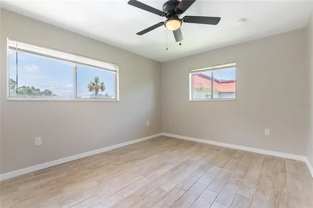 an empty room with wooden floor ceiling fan and windows