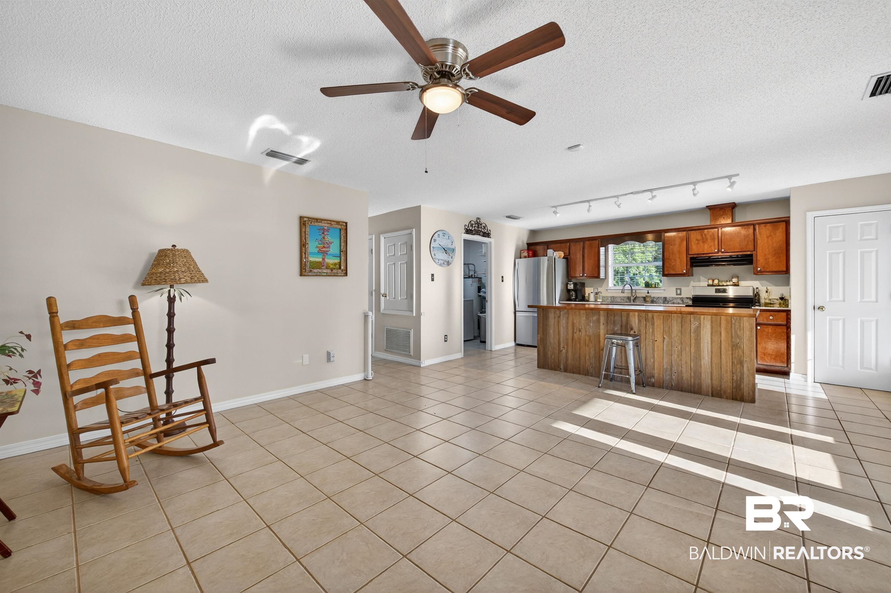 9624 North Bay Street Foley, AL 36535 - Photo 8 of 59 Open-concept living space featuring neutral wall tones, large format tile flooring, a ceiling fan with integrated lighting, a kitchen island with wood-finish paneling, and wood-finish cabinetry