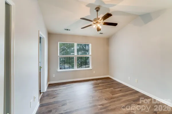 an empty room with wooden floor fan and windows
