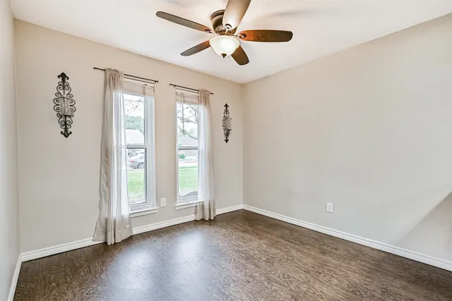 an empty room with wooden floor fan and windows