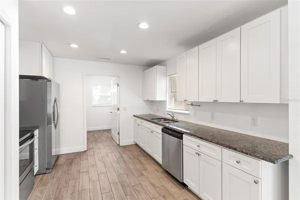 a kitchen with stainless steel appliances granite countertop a refrigerator a sink dishwasher and white cabinets with wooden floor