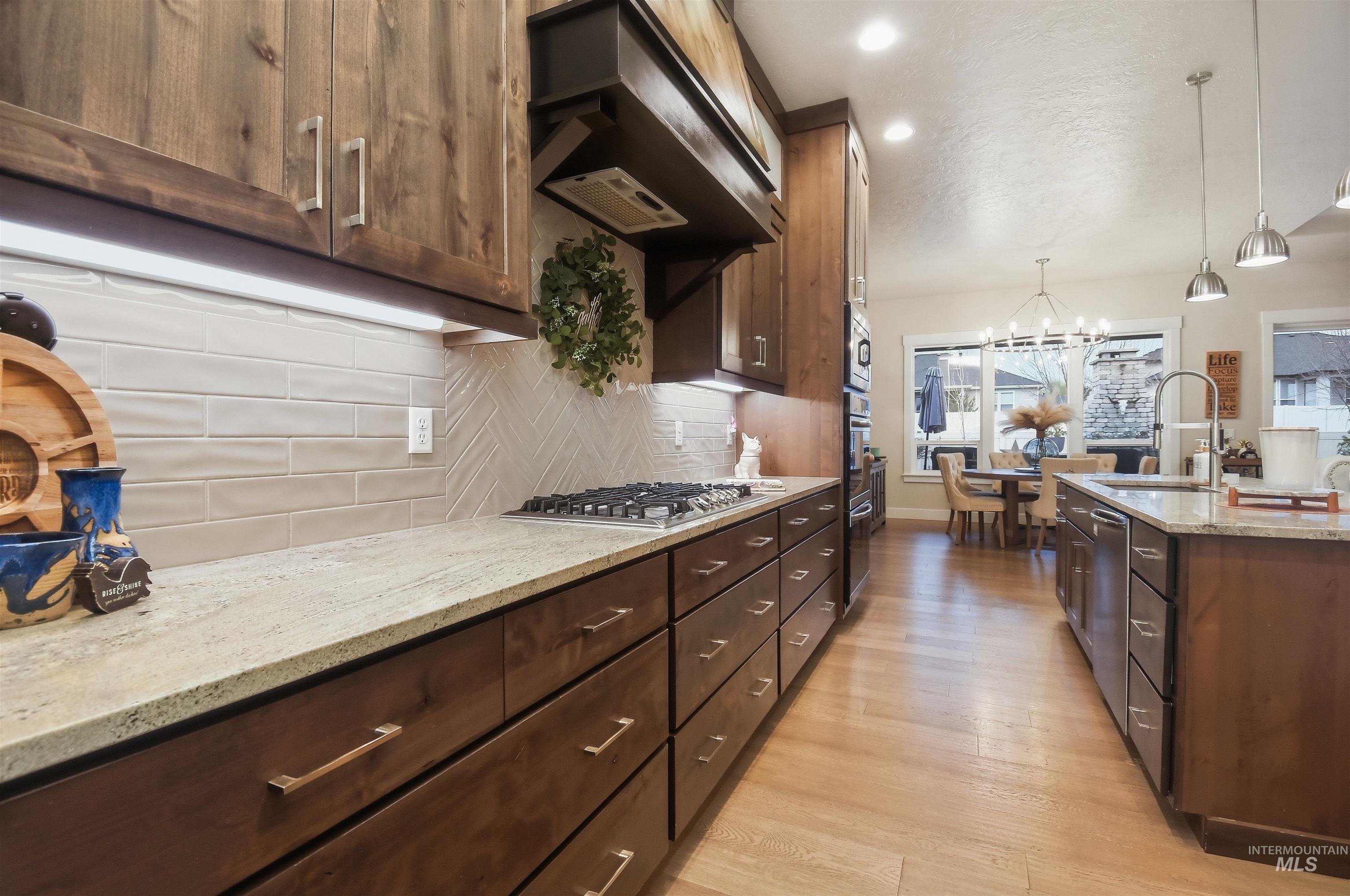 12174 West Lacerta Street Star, ID 83669 - Photo 14 of 49 Kitchen with light stone counters, light wood-type flooring, a chandelier, dark wood finish cabinets, and stainless steel appliances