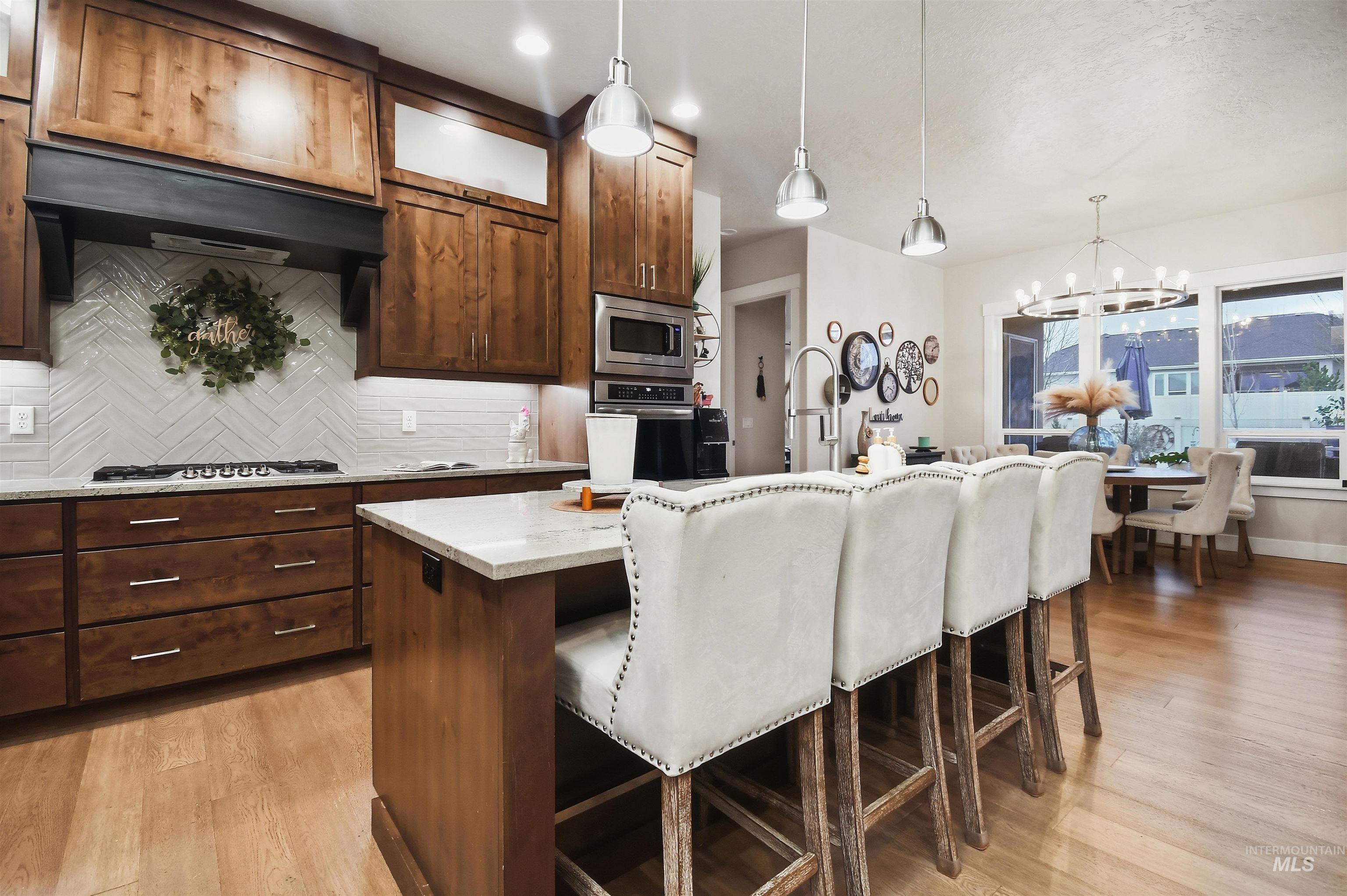 12174 West Lacerta Street Star, ID 83669 - Photo 15 of 49 Kitchen with a center island with sink, light stone countertops, a kitchen bar, hanging lights, and stainless steel appliances