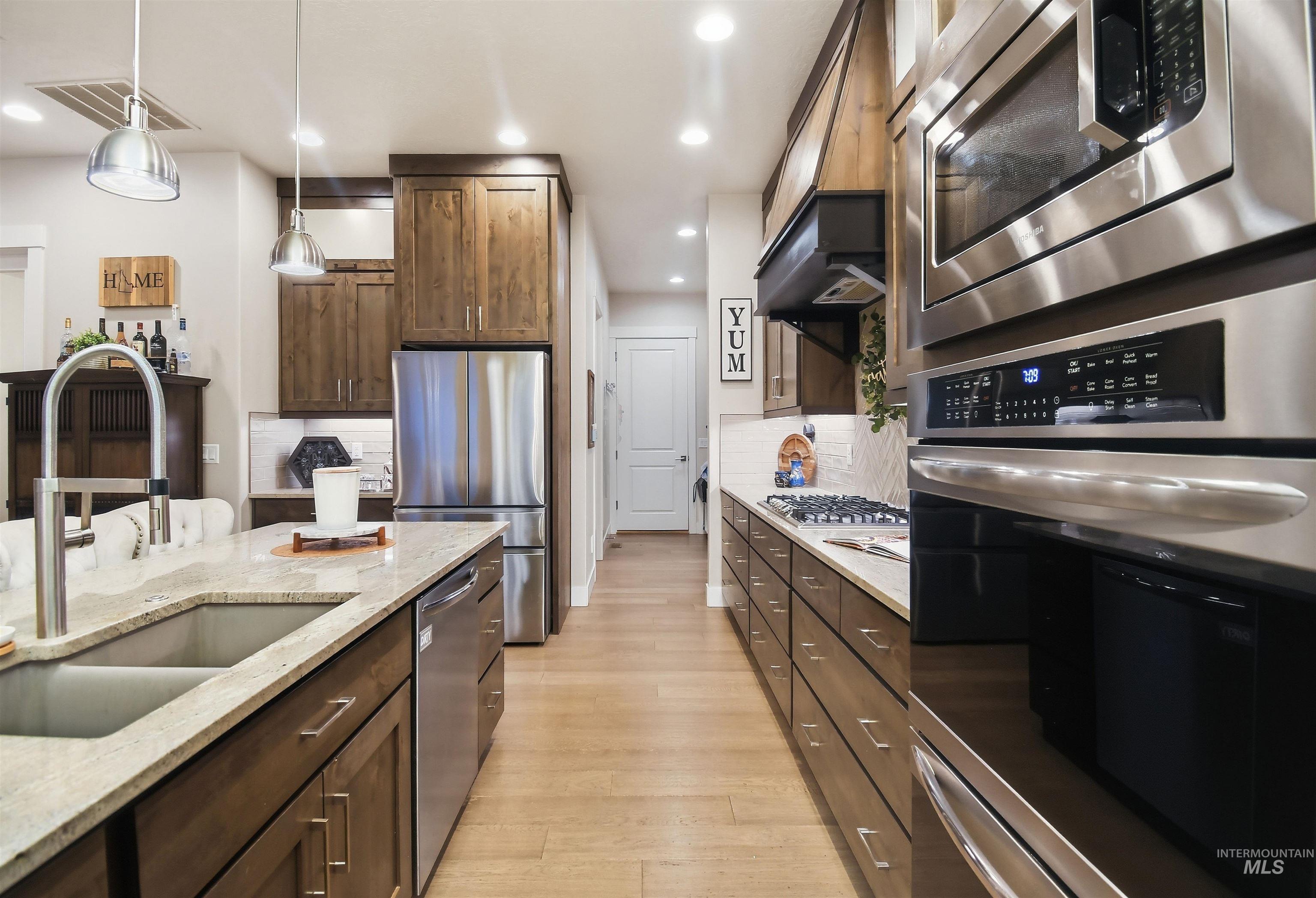 12174 West Lacerta Street Star, ID 83669 - Photo 19 of 49 Kitchen featuring stainless steel appliances, light stone countertops, light wood-style floors, and dark wood finish cabinetry