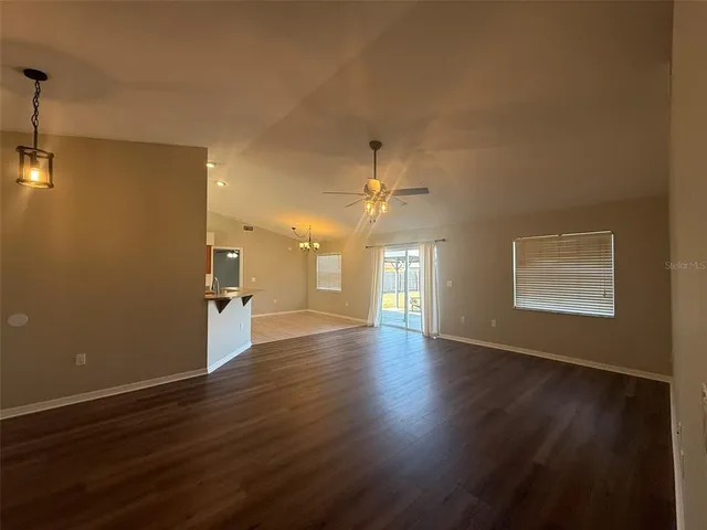 an empty room with wooden floor chandelier fan and windows