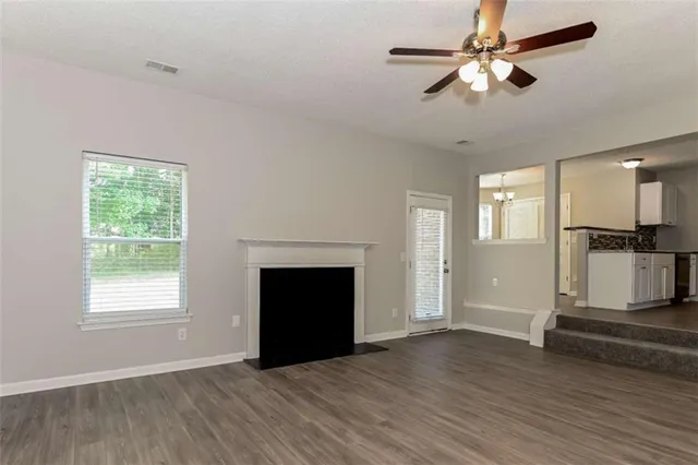 an empty room with windows a fireplace a ceiling fan and wooden floor