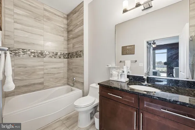 a bathroom with a granite countertop bathtub shower sink vanity mirror and toilet
