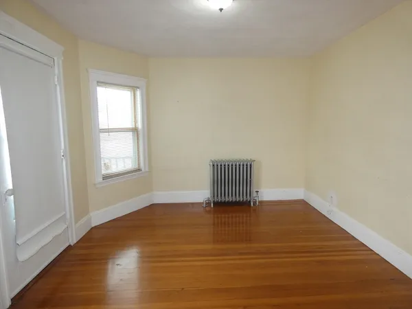 a view of an empty room with a window and wooden floor