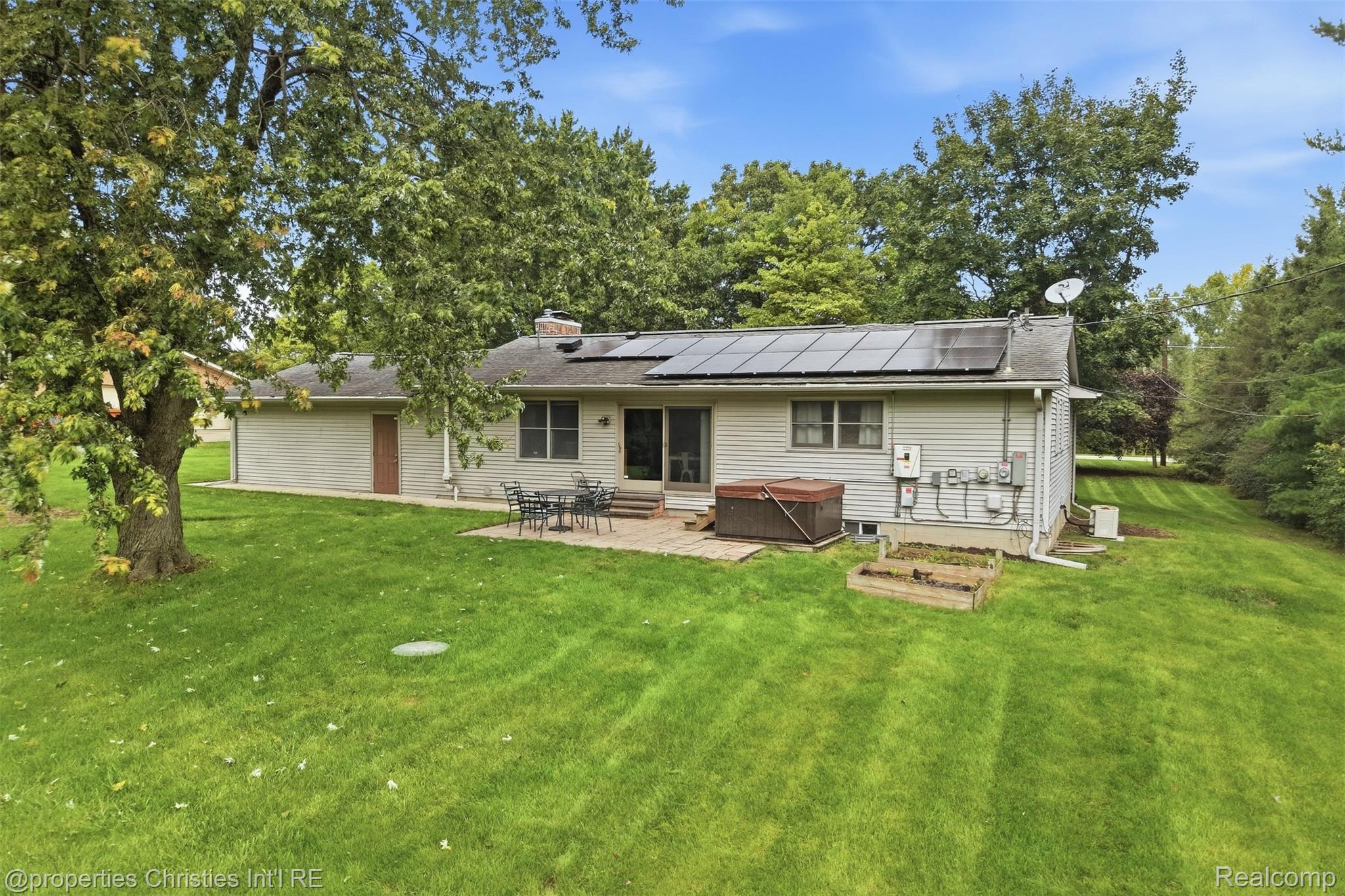 4030 Textile Road Ypsilanti, MI 48197 - Photo 53 of 58 Rear exterior featuring solar panels, a patio area, a raised garden bed, and mature trees