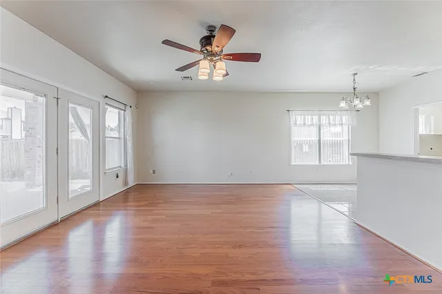 an empty room with wooden floor chandelier fan and windows
