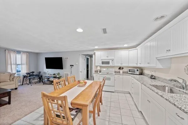 a kitchen with stainless steel appliances kitchen island granite countertop a stove top oven a sink a dining table and chairs with white cabinets
