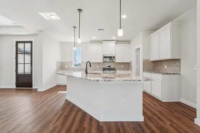 a kitchen with kitchen island a stove a sink a refrigerator and white cabinets with wooden floor