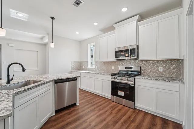 a kitchen with stainless steel appliances granite countertop a stove top oven a sink and white cabinets with wooden floor