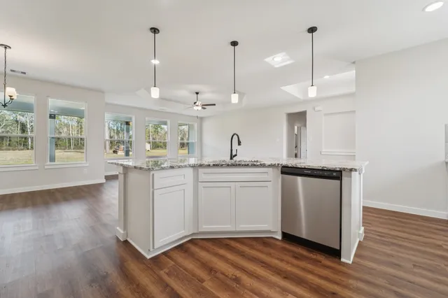 a kitchen with stainless steel appliances granite countertop a stove a sink a refrigerator and white cabinets with wooden floor