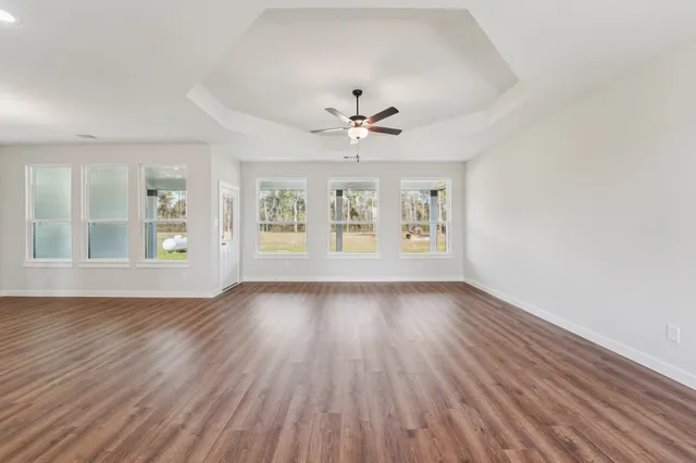 an empty room with wooden floor chandelier fan and windows