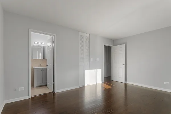 a view of an empty room with wooden floor and a bathroom