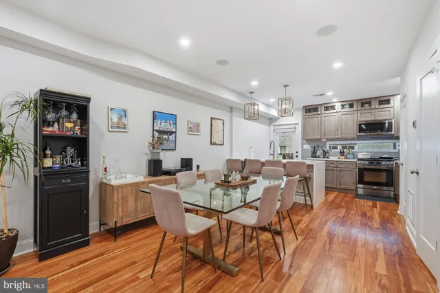 a kitchen with stainless steel appliances kitchen island granite countertop a refrigerator a stove a microwave oven a dining table and chairs with wooden floor