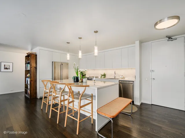 a kitchen with stainless steel appliances kitchen island granite countertop a refrigerator a stove a dining table and chairs with wooden floor