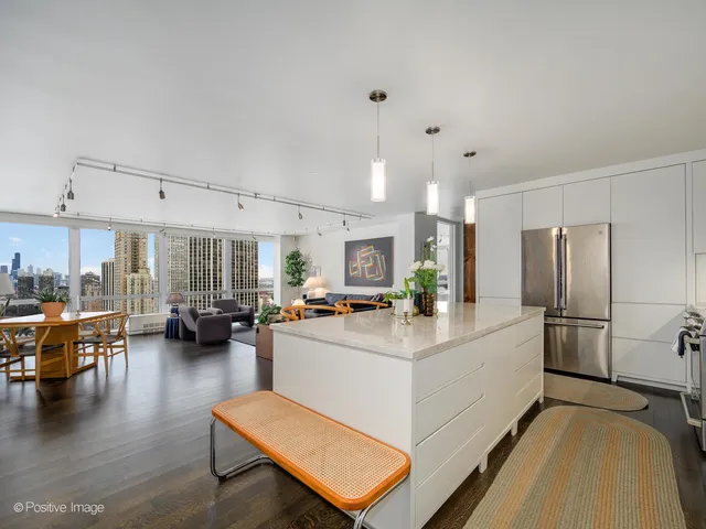 a kitchen with stainless steel appliances kitchen island granite countertop a refrigerator a stove a dining table and chairs with wooden floor