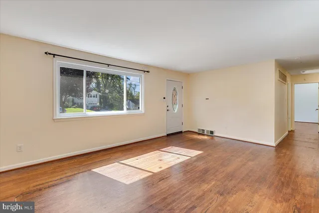 a view of an empty room with wooden floor and a window