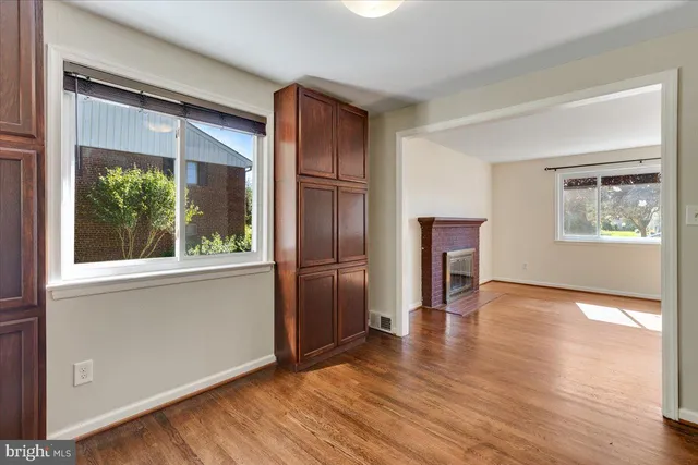 an empty room with wooden floor kitchen view and windows