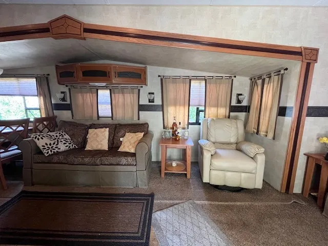 a living room with stainless steel appliances furniture a rug and a kitchen