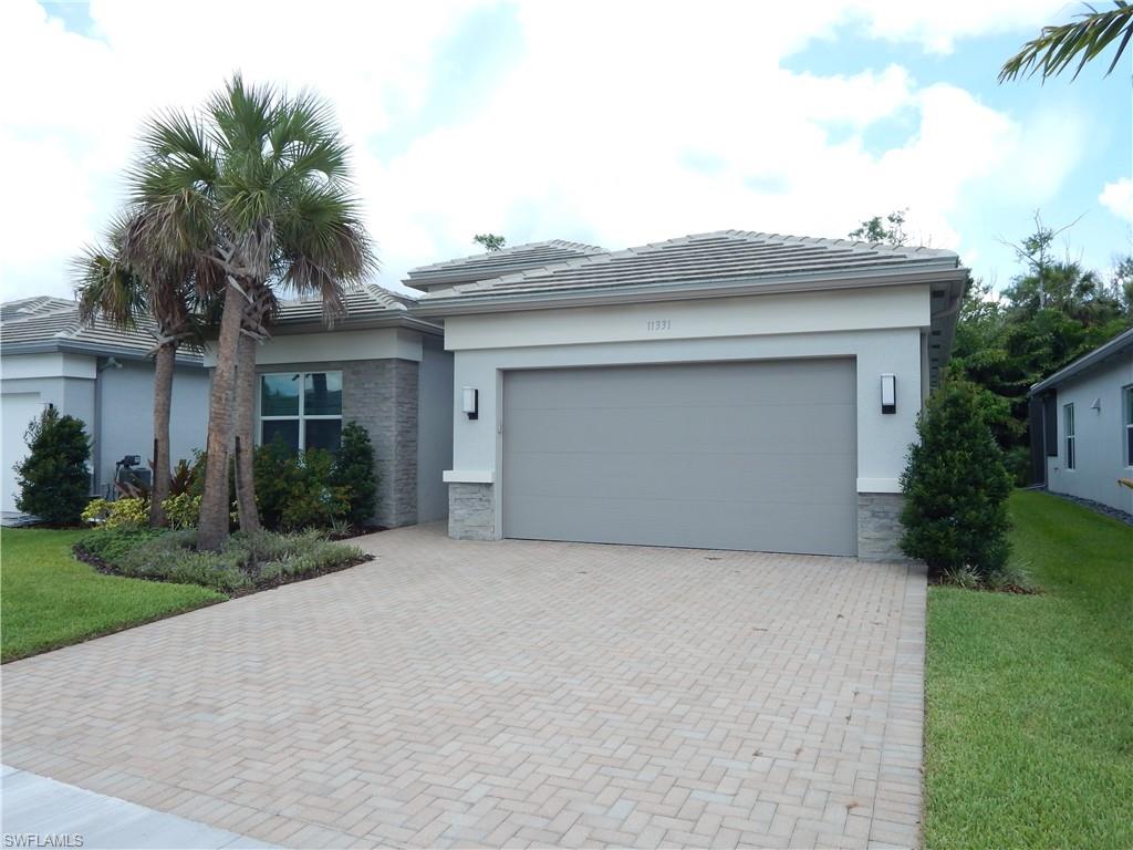 11331 Jacaranda Drive Naples, FL 34120 - Photo 1 of 47 View of front facade featuring stucco siding, stone siding, decorative driveway, a garage, and a front lawn