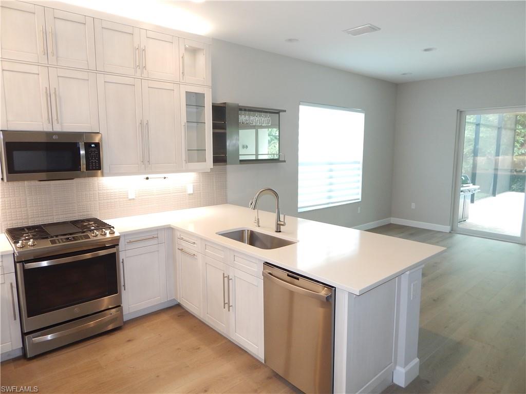 11331 Jacaranda Drive Naples, FL 34120 - Photo 11 of 47 Kitchen featuring stainless steel appliances, a sink, a peninsula, light wood finished floors, and backsplash