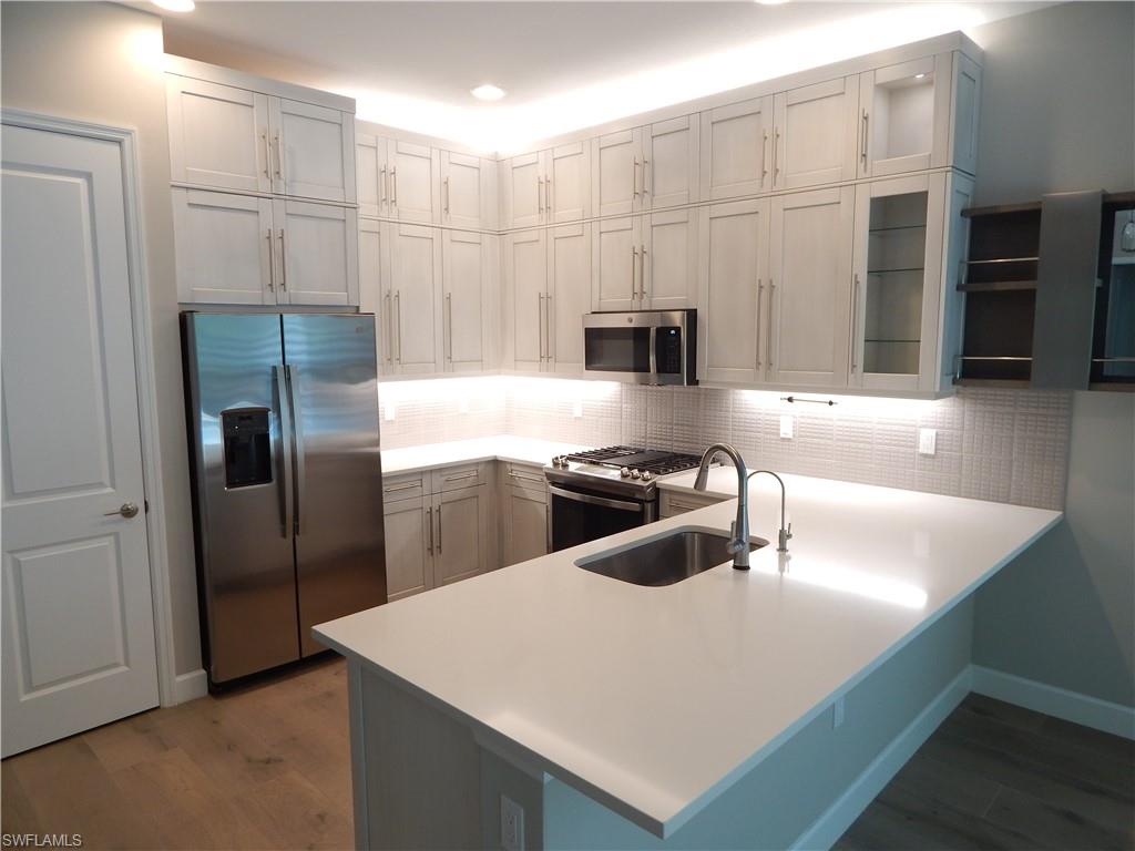 11331 Jacaranda Drive Naples, FL 34120 - Photo 7 of 47 Kitchen with appliances with stainless steel finishes, a sink, a peninsula, wood finished floors, and glass insert cabinets