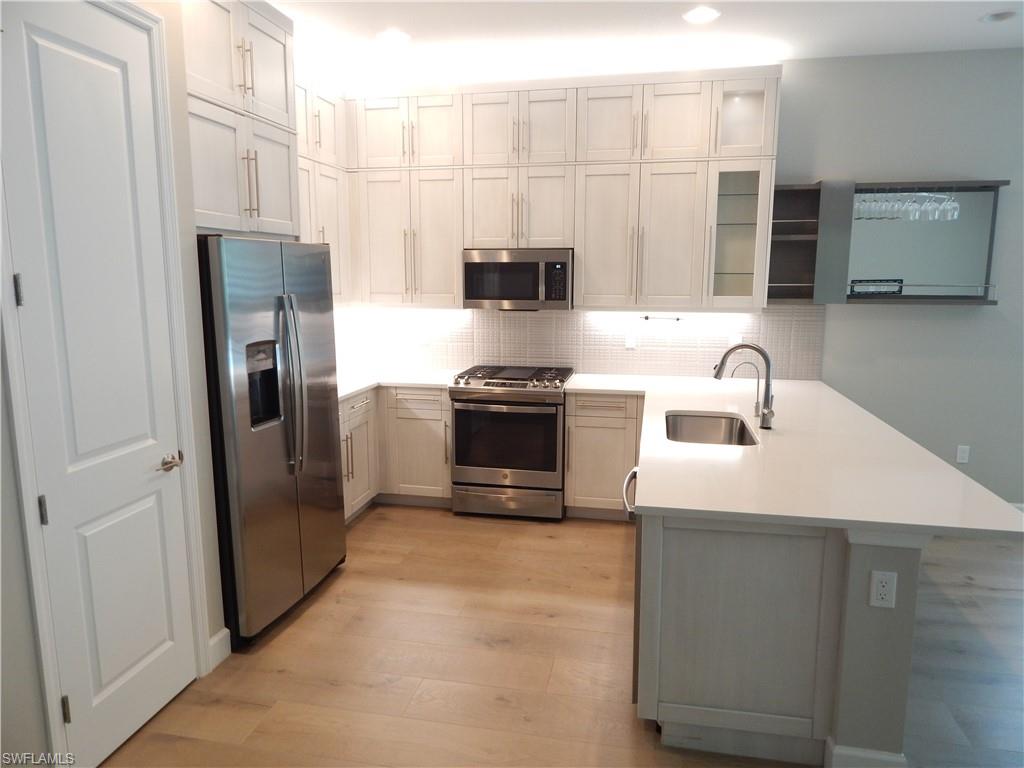 11331 Jacaranda Drive Naples, FL 34120 - Photo 8 of 47 Kitchen featuring stainless steel appliances, a sink, a peninsula, light wood-style flooring, and tasteful backsplash